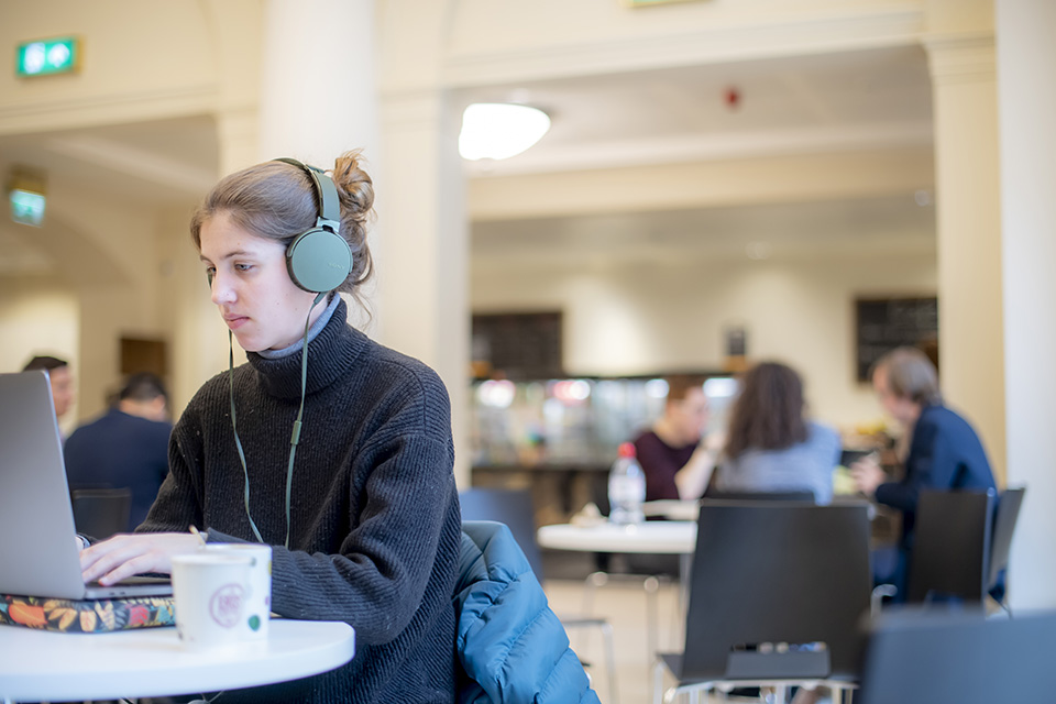 A student working on laptop with headphones on, in the RCM cafe